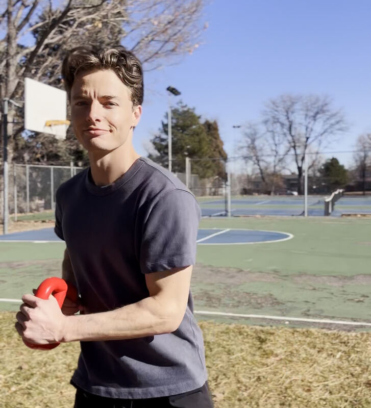 Tanner smiling on an outdoor basketball court, holding a red training bell.