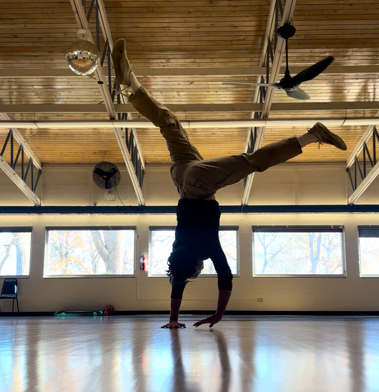 Tanner mid one-armed handstand in a sunlit studio, legs scissored beneath a disco ball.